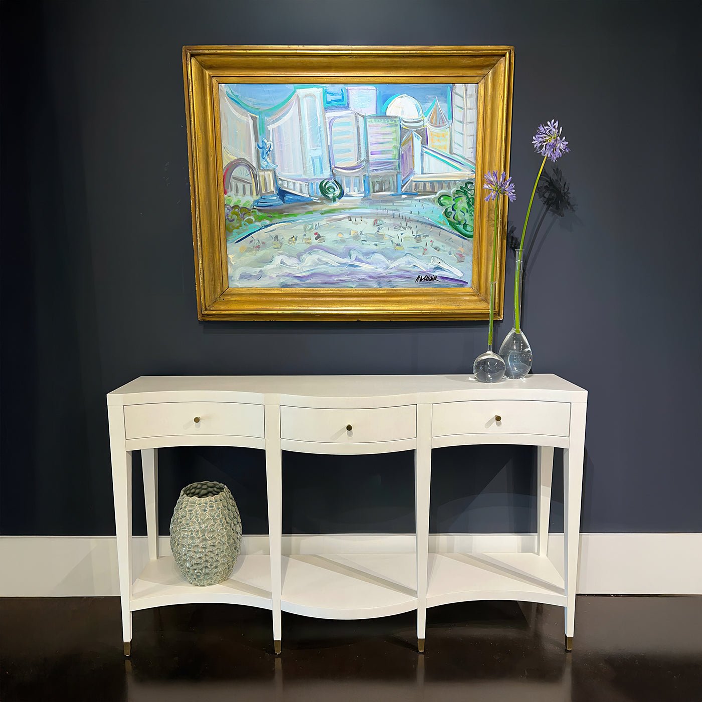 Curved console table under framed artwork, decorative display setup.