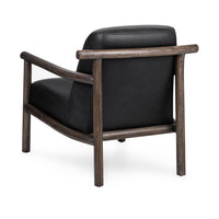 Rear three-quarter view of the black leather chair showing its rounded wood back rail