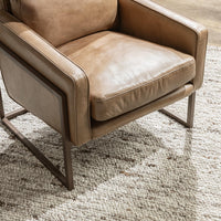 Tan leather chair seat detail showing piped cushions, padded arms and the iron frame