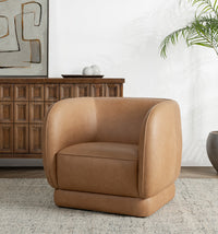 Tan leather barrel-back swivel chair styled beside a wood cabinet and potted palm