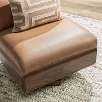 Tan leather swivel chair seat and walnut base detail, styled with a patterned throw pillow