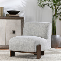 Ivory armless accent chair styled on a pale rug beside a cabinet and potted palm