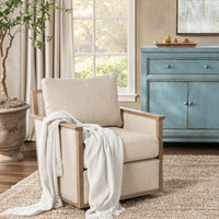 Natural ash-frame swivel chair styled with a pale throw beside a window and blue cabinet