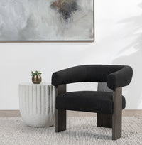 Charcoal curved-back accent chair styled beside a ribbed round table beneath wall art