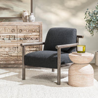 Charcoal wood-arm chair styled beside a small pedestal table and carved cabinet