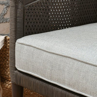 Close-up of the gray chair's piped seat cushion beside the woven rattan side