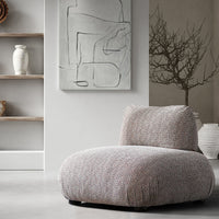 Armless upholstered chair styled beneath abstract artwork beside open shelves