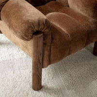 Bronze chair arm and channel-tufted seat detail above an oak leg, styled on a rug