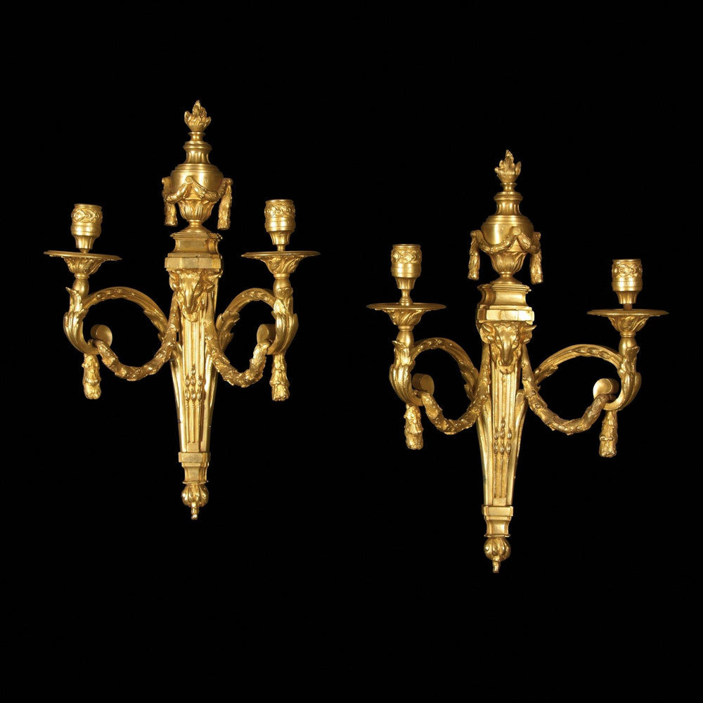 Pair of Louis XVI gilt bronze sconces on black background.