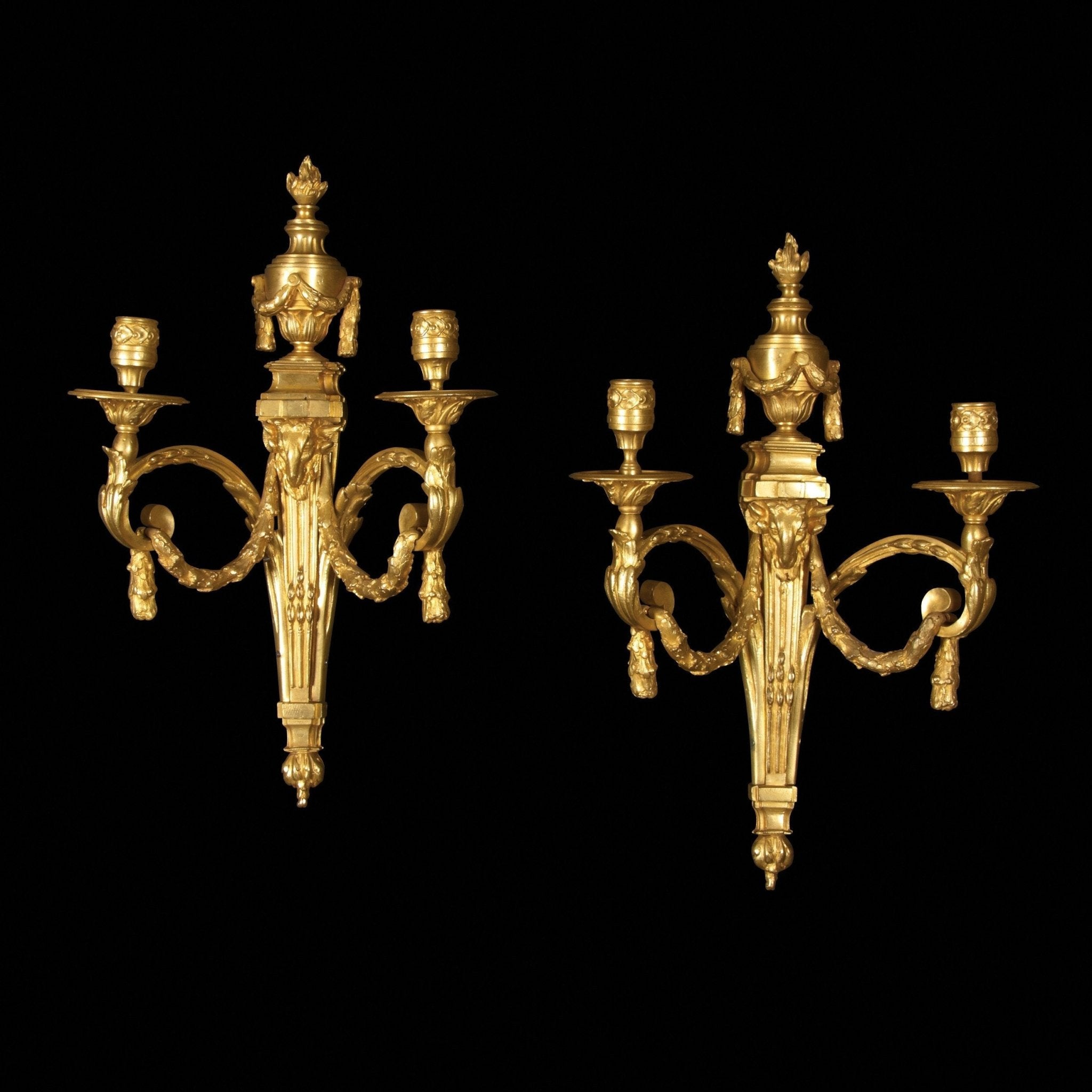 Pair of Louis XVI gilt bronze sconces on black background.
