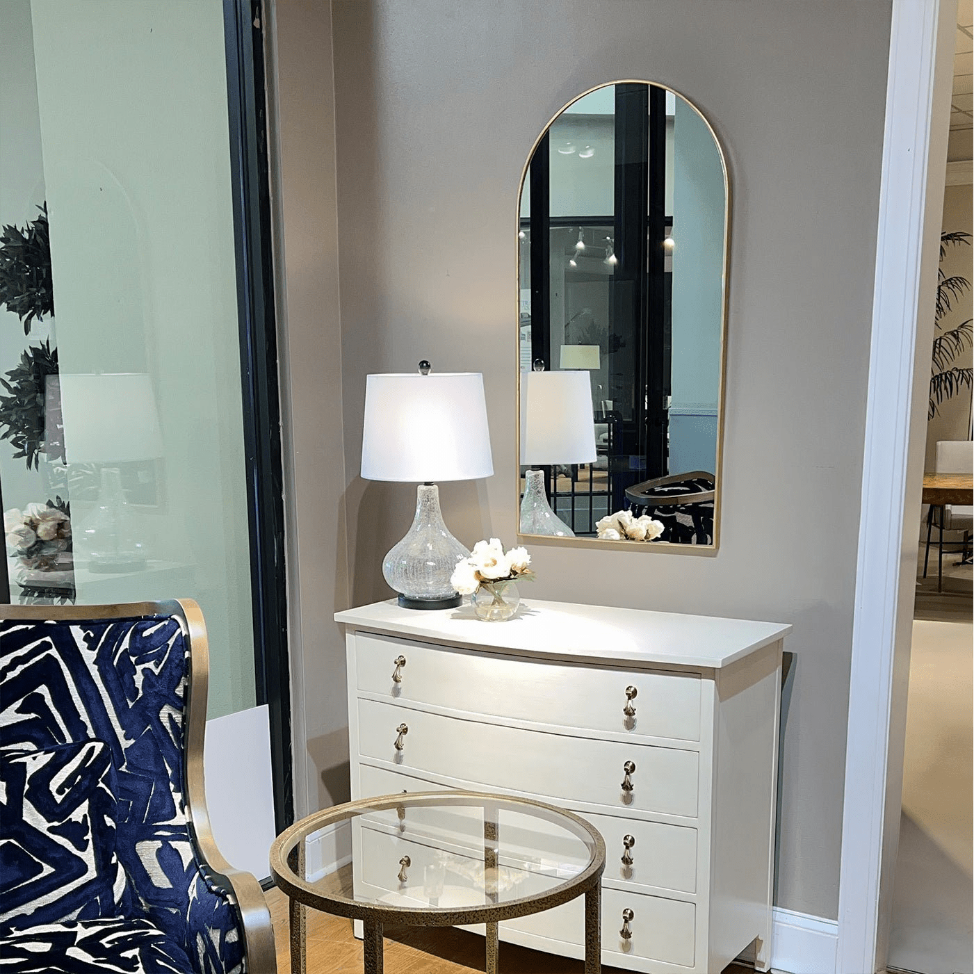 Arch mirror above white dresser in decorated room.