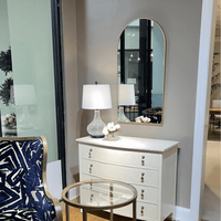 Arch mirror above white dresser in decorated room.