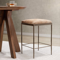 Tan backless hair-on-hide counter stool beside a wood counter table on a light rug.