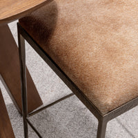 Overhead detail of the tan hair-on-hide seat and iron frame beside a wood table.