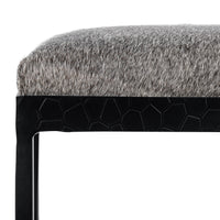 Close-up of the gray hair-on-hide seat edge and textured black iron apron on the backless counter stool.