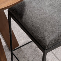 Overhead detail of the gray hair-on-hide seat and black iron frame beside a wood table.