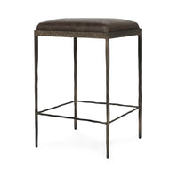 Three-quarter view of dark brown backless leather counter stool with a square padded seat and iron footrails.