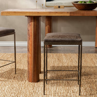 Dark brown backless leather counter stool at a wood counter table on a woven rug.
