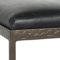 Close-up of the black leather seat corner and textured iron apron on the backless counter stool.