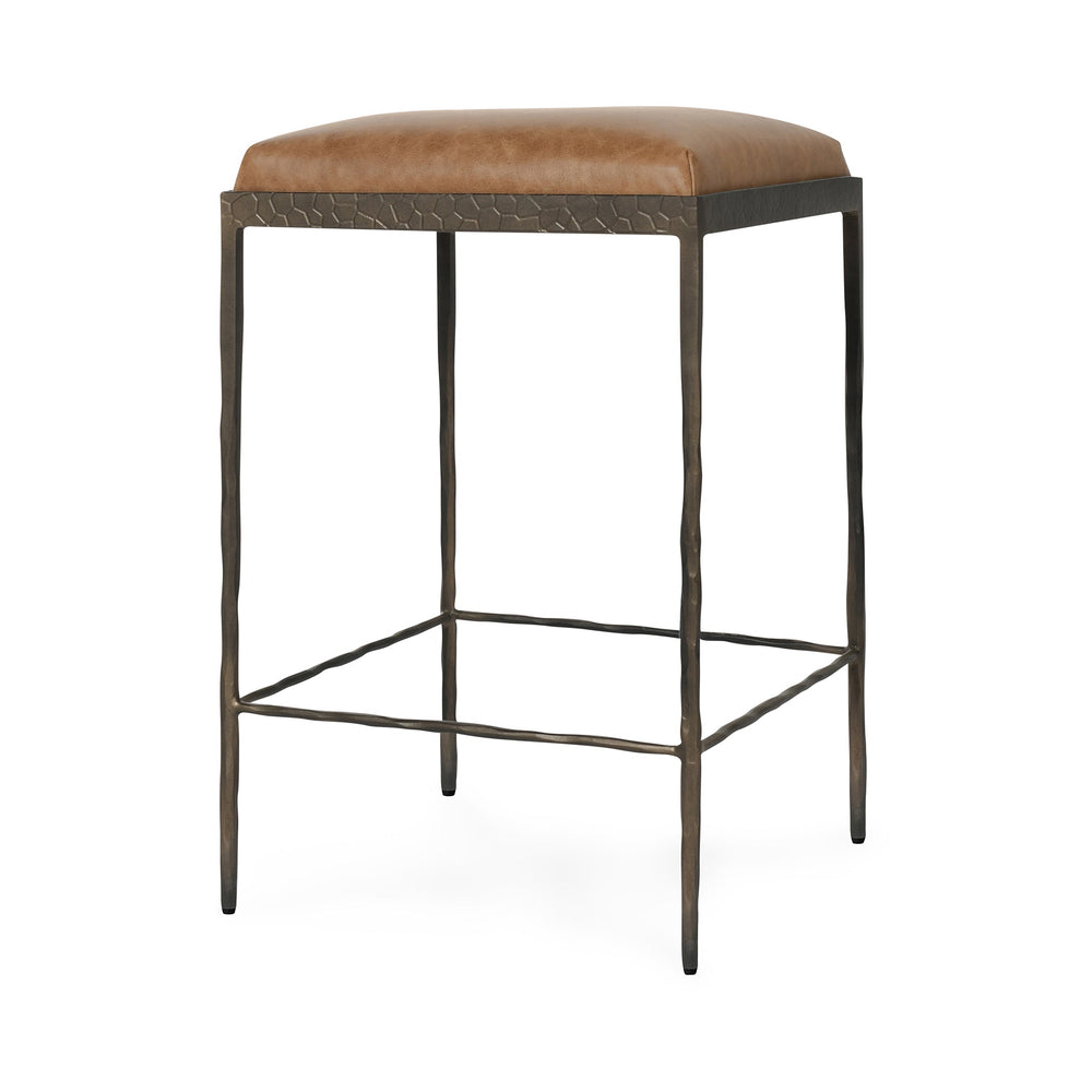 Three-quarter view of tan backless leather counter stool with a square padded seat and iron footrails.
