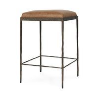 Three-quarter view of tan backless leather counter stool with a square padded seat and iron footrails.