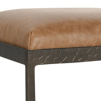 Close-up of the tan leather seat corner and textured iron apron on the backless counter stool.