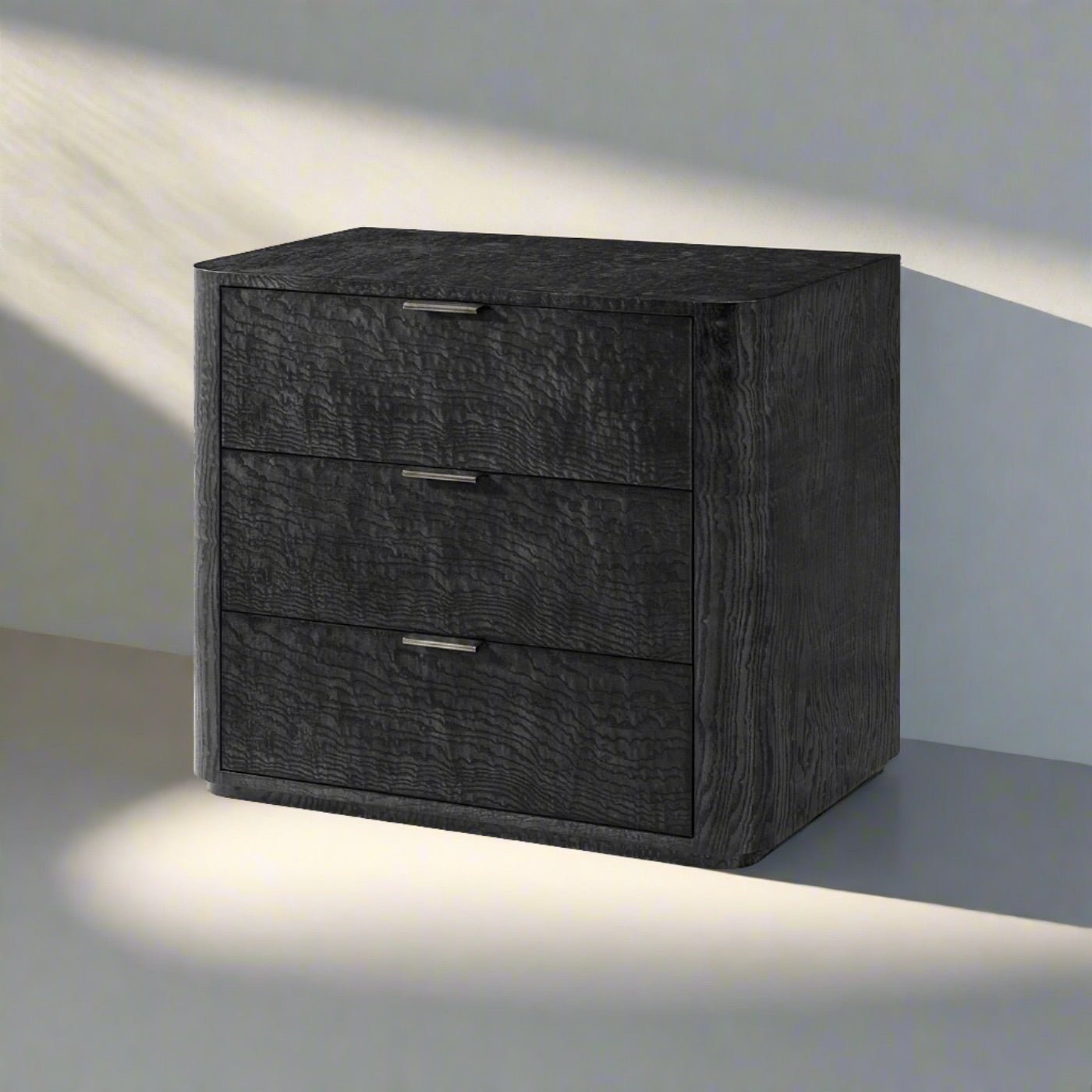 Black Art Deco nightstand, shadowed lighting, three drawers.