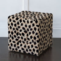 Black ocelot cube ottoman on dark floor, front view.