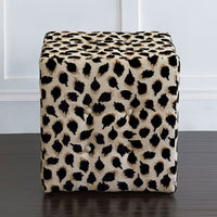 Black ocelot cube ottoman centered against white wall.