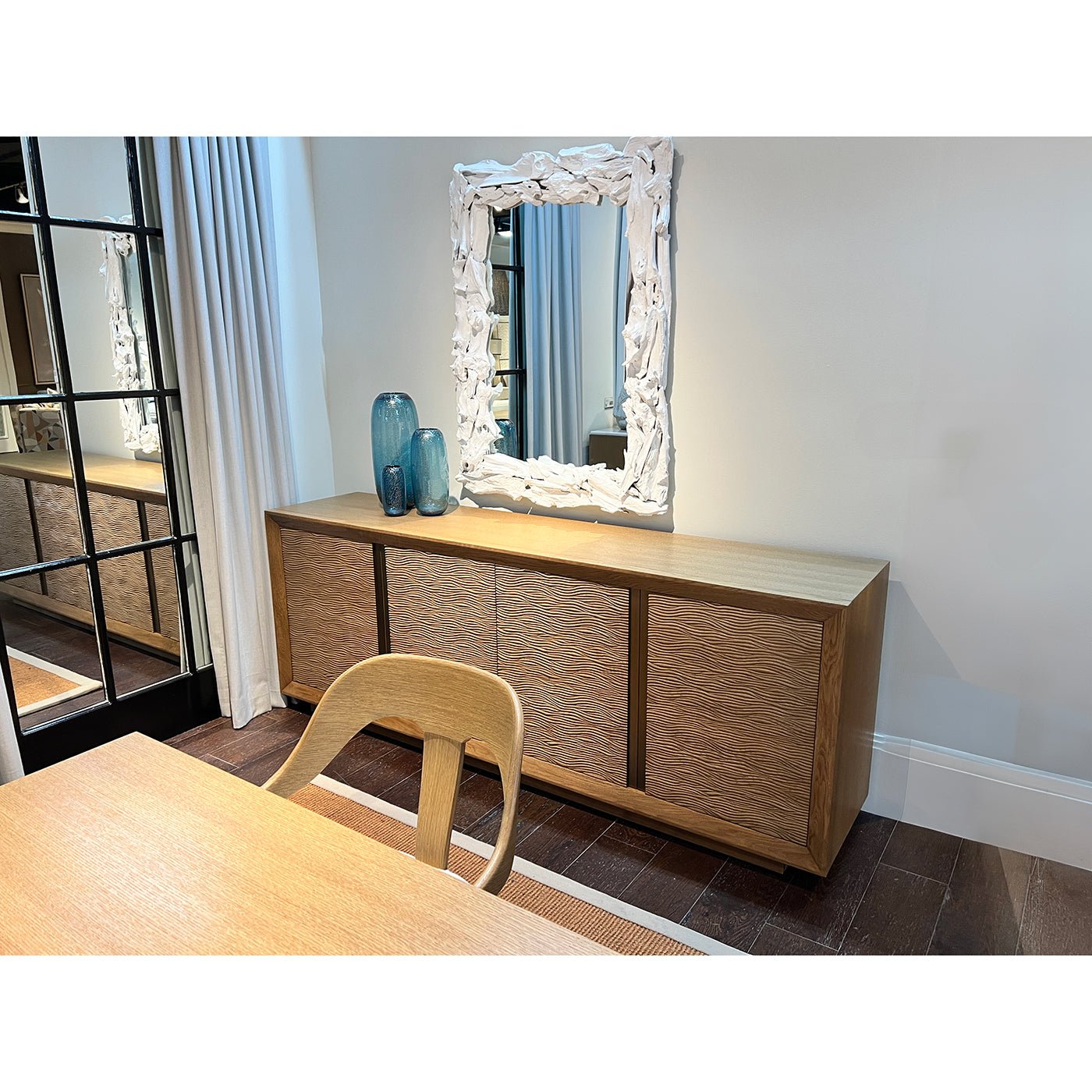 Wooden media cabinet under decorative mirror with vases.