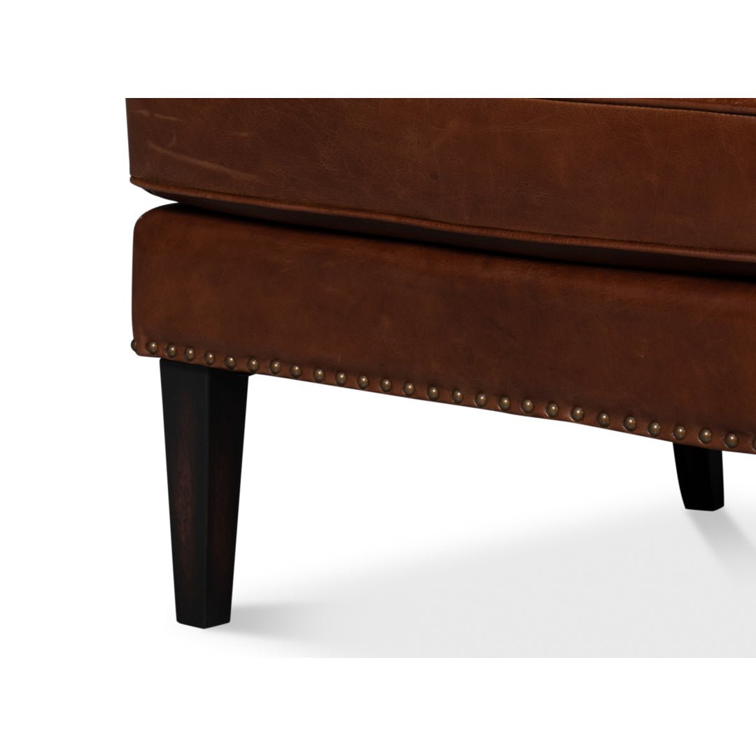 Brown leather wing chair, leg and seat detail.