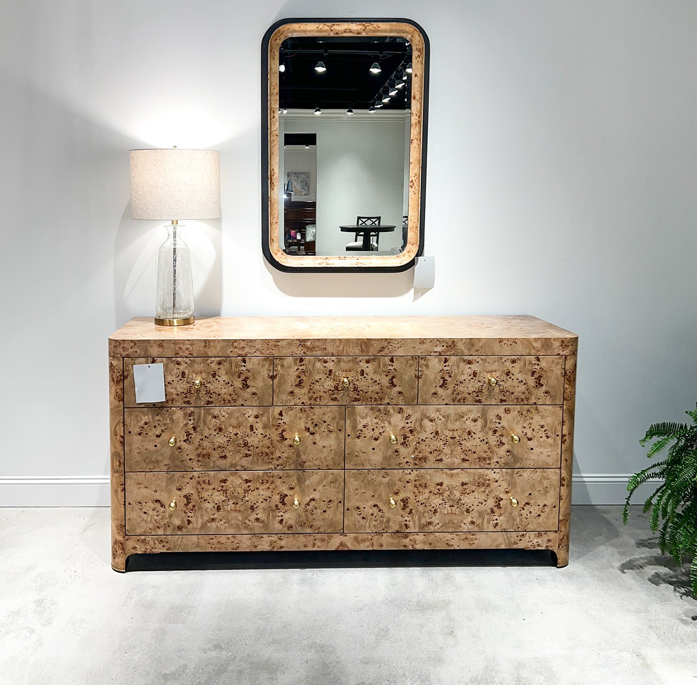 Mirror above dresser, lamp, reflection of furniture showroom.