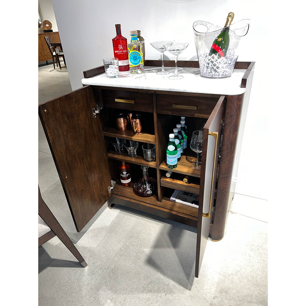 Open burl wood bar cabinet stocked with bottles and glasses.