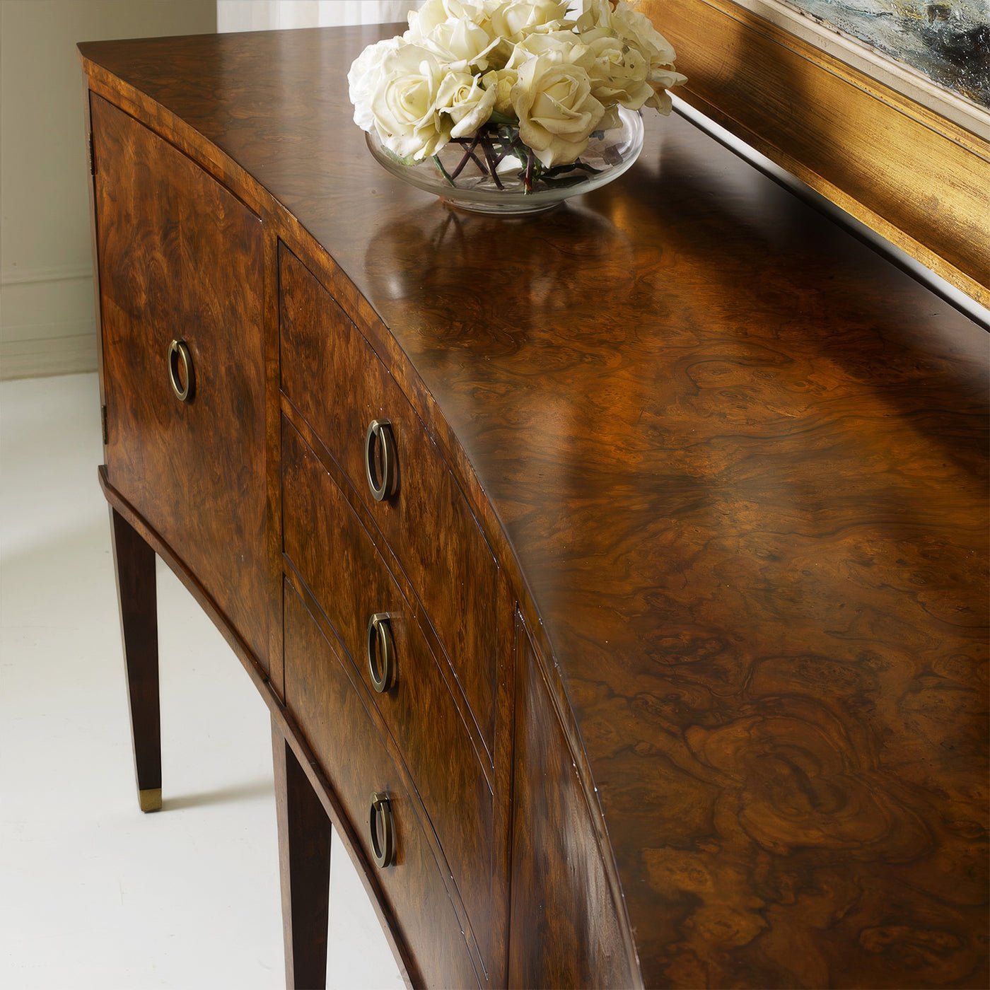 Curved top of burl wood sideboard with decorative vase.
