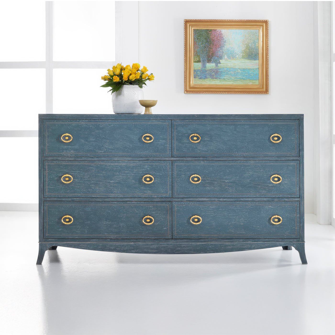 Blue dresser in bright room with artwork and flowers.