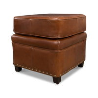 Angled view of ottoman emphasizing leather texture and trim.