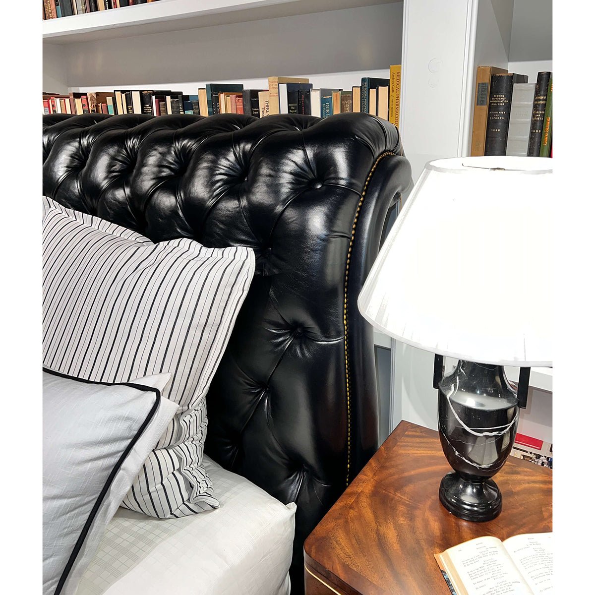 Headboard of classic tufted leather king bed with books.