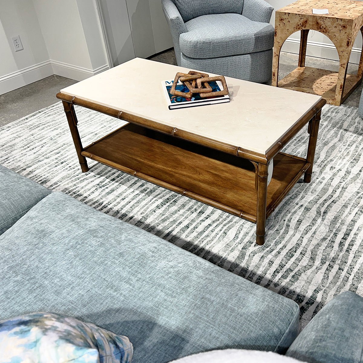 Bamboo coffee table on striped rug with blue sofa.