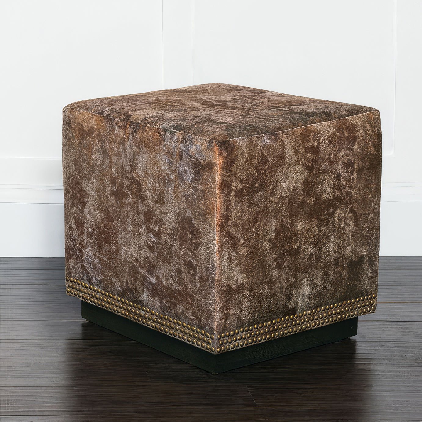 Copper velvet ottoman on dark wood flooring, angled view.