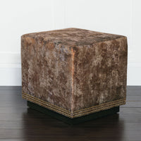 Copper velvet ottoman on dark wood flooring, angled view.