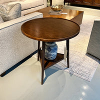 Wooden side table in living room setting, ornate vase beneath.