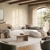 Cream curved sectional styled with accent pillows and a throw around a stone-look coffee table