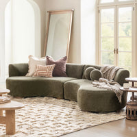 Olive green curved sectional styled with pillows and a throw beside tall windows and a leaning mirror