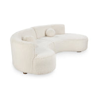 Angled view of cream curved sectional showing its rounded end, low back and plush upholstery