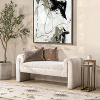 Ivory textured upholstered bench styled with two brown pillows beneath abstract artwork beside nesting tables