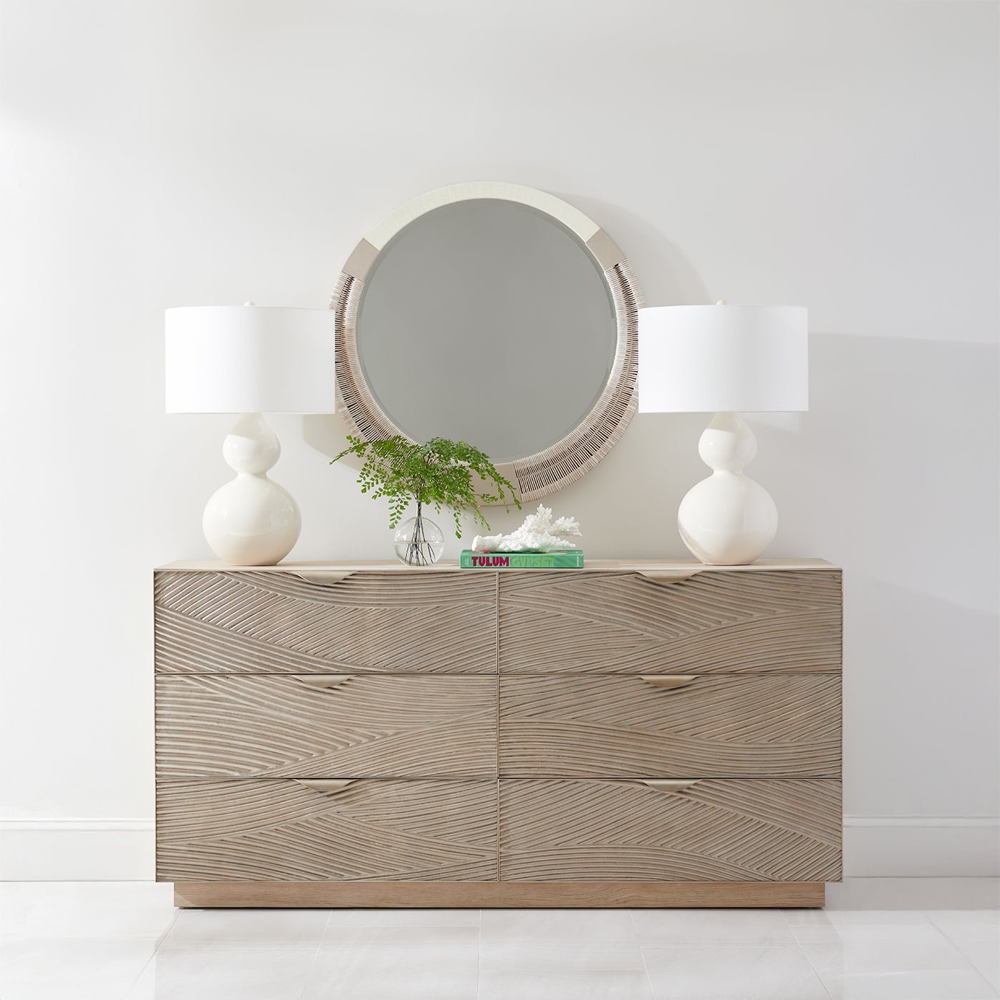 Dresser topped with modern round mirror and lamps.