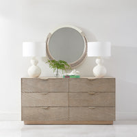 Dresser topped with modern round mirror and lamps.