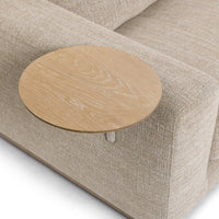 Angled close-up of the round wood table above the beige sectional arm