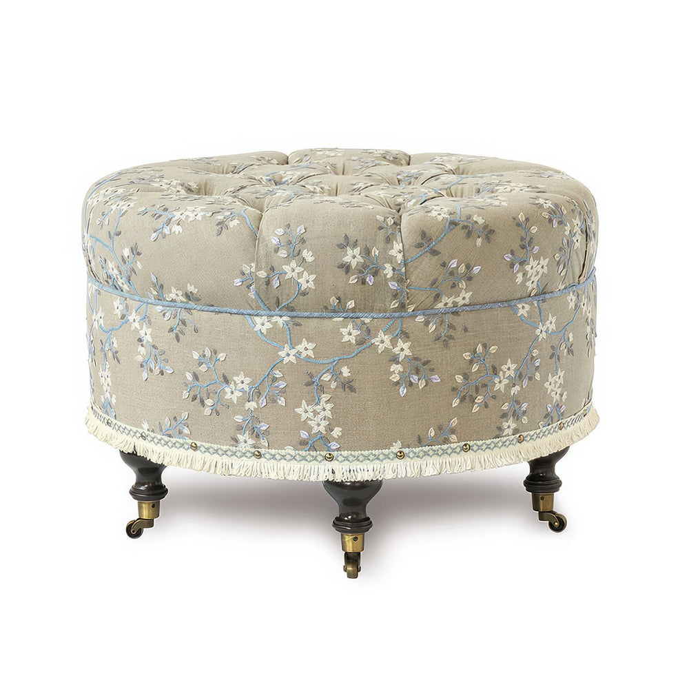 Beige embroidered round poof on casters, close-up view.