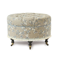 Beige embroidered round poof on casters, close-up view.
